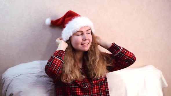 Young woman is putting on santa hat sitting in bed