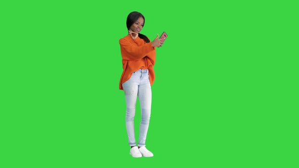 Smiling African American Woman in Bright Jumper Taking Selfie and Checking Her Phone on a Green