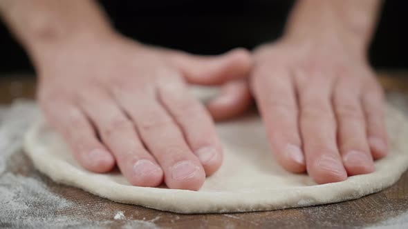 Cook Stretches Pizza Dough Edge on the Wooden Table in the Dark Kitchen