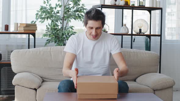 Caucasian Man Millennial Customer Buyer Sitting on Couch Rubs Palms Waiting for Gift Opens Unpacks