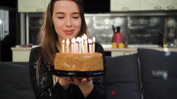 A Young Caucasian Lady is Sitting at Home on the Sofa on Her Head Wearing a Birthday Cap and Holding