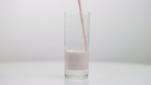 Pink Healthful Fruit Yogurt Pouring in Transparent Glass Closeup