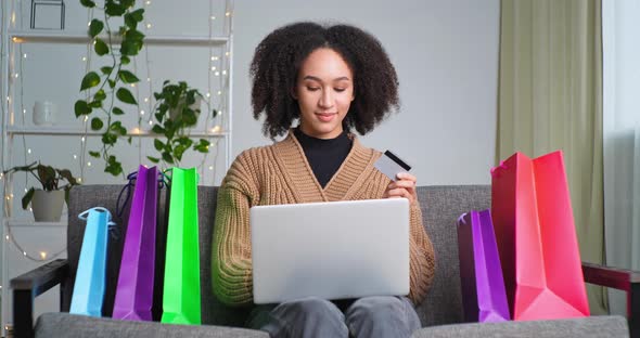 Beautiful Happy African American Woman Sitting on Couch at Home Picking Up New Clothes in Online