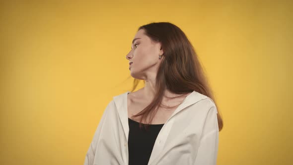 Young Adult Caucasian Woman is Shaking Her Hair and Looking at Camera on Bright Yellow Background