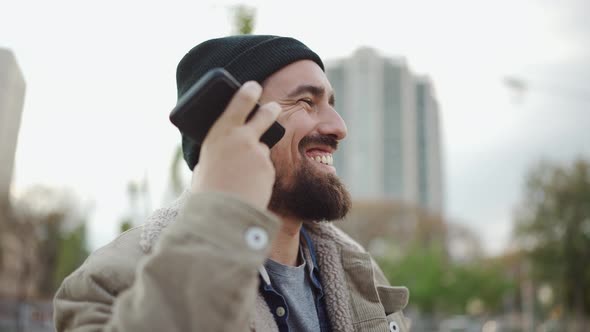 Laughing bearded man wearing hat listening voice message by phone