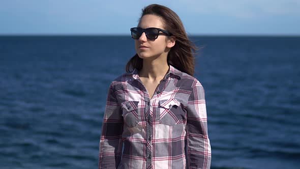 A Young Woman on a Background of the Sea, Girl in Sunglasses in Sunny Weather, Explores the Nature