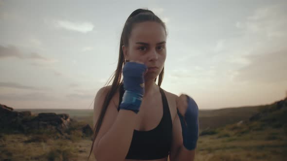 Woman in Sports Uniform and with Bandages on Her Hands Practices Boxing Punches Looking Into Camera