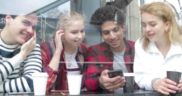 Happy multiracial friends looking at a smartphone in a cafe and laughing