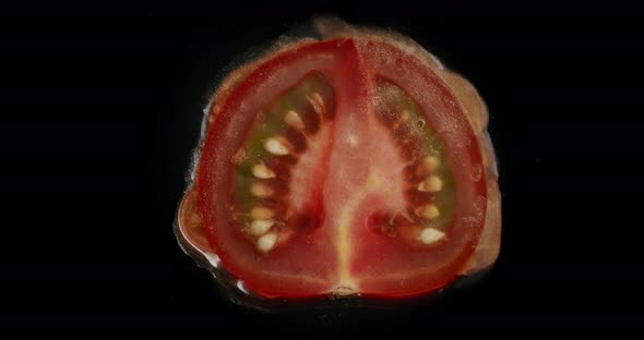 Top shot of a tomato getting squished. Oil and water gets pushed out of the fruit.