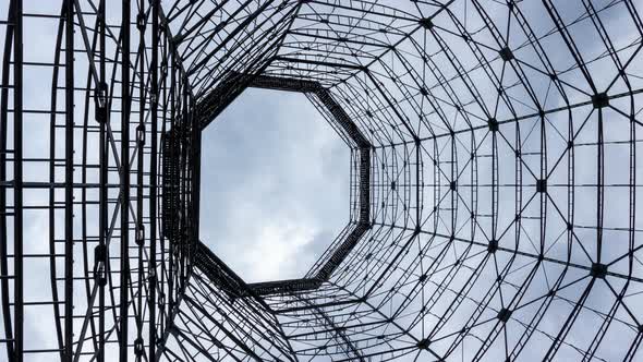 Looking up through geometric frame of abandoned cooling tower, cloudscape time lapse