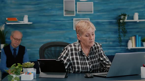 Multitasking Retired Woman Reading on Laptop and Tablet in Same Time