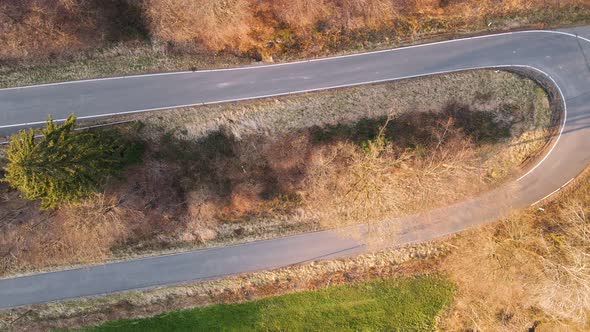 Motorcycle rider driving up a switchback road at sunset. Top down rotating aerial view