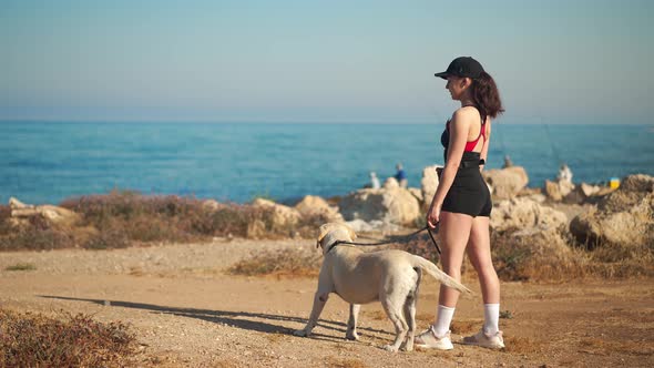 Wide Shot Confident Young Woman Pointing Away Standing with White Labrador on Mediterranean Sea