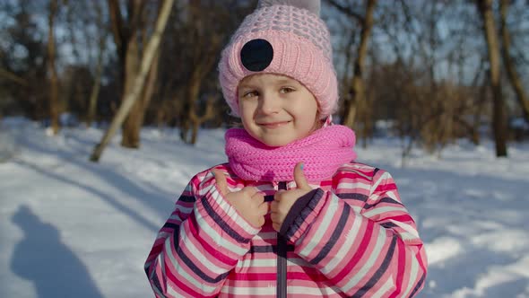 Child Girl Smiling Showing Ok Sign Thumbs Up Gesture on Snowy Road in Winter Sunny Park Forest