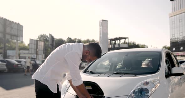 Young Arab Man Recharging White Electric Car at Parking Lot