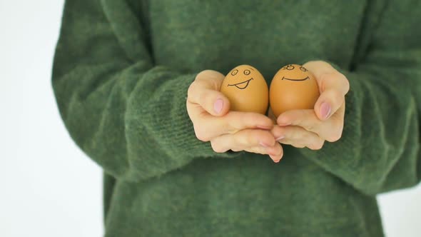 Young Female in Green Sweater is Showing Eggs with Hand Drawn Face with a Smile From Straw Basket