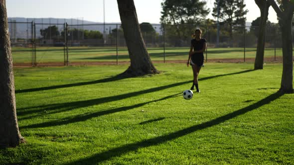 A female soccer player kicking a football to her teammate on a grass sport field in slow motion.