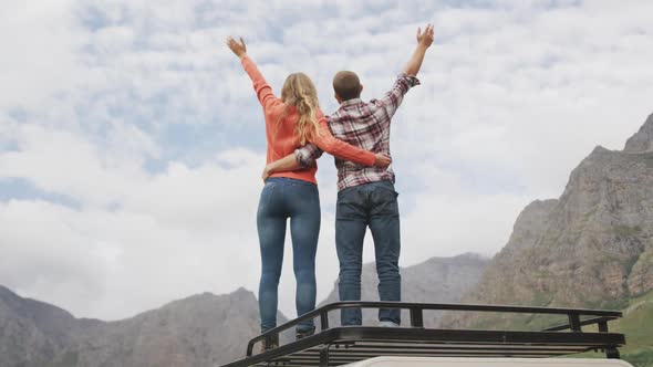 Caucasian couple having a good time on a trip to the mountains, embracing and raising their hands