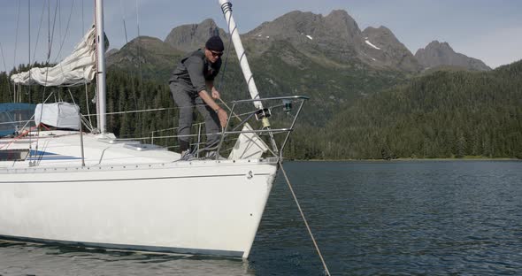 Sailing in Alaska. Man Pulling Rope at Bow of Sailboat With Scenic Coastline in Basckground, Slow Mo