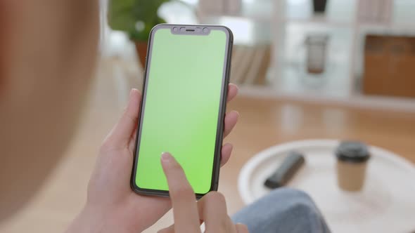 Woman holding mockup smartphone green screen with type message on the sofa at home.