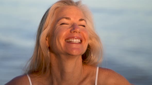 Blonde mature woman breaking up and laughing looking at the camera in a portrait.