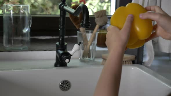 Woman washing yellow pepper under water at kitchen