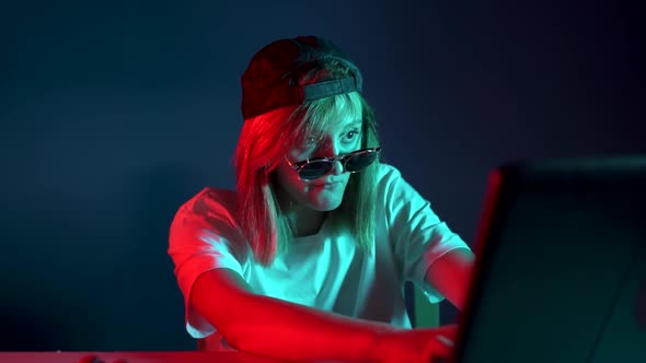 Girl Gamer with Glasses Sitting at a Laptop and Typing Something