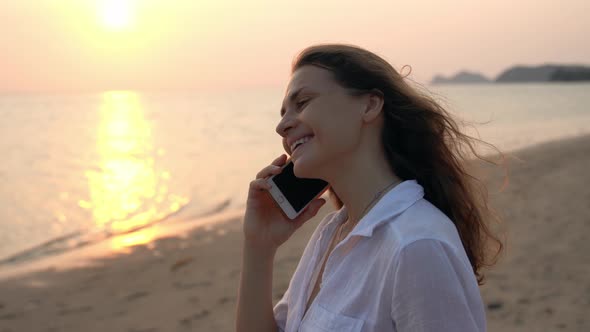 A Young Woman Is Standing on the Beach Smiling and Talking on the Phone