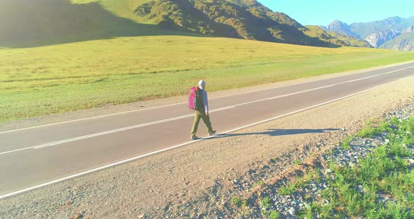 Flight Over Hitchhiker Tourist Walking on Asphalt Road. Huge Rural Valley at Summer Day