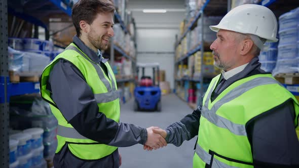 Satisfied Senior Man Shaking Hands with Young Smiling Warehouse Employee Indoors and Leaving