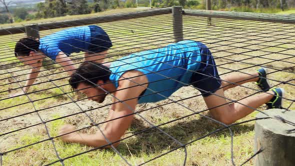 Fit man and woman crawling under the net during obstacle course