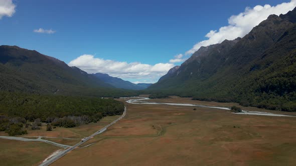 Cars travelling through a beautiful mountain valley with river and large open grass fields in Fiordl