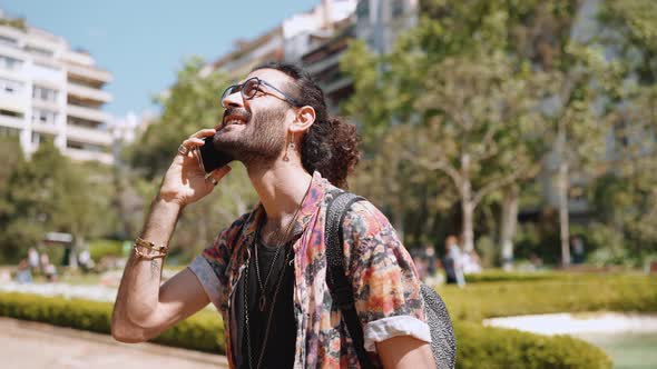 Smiling curly-haired bearded man in eyeglasses talking on phone