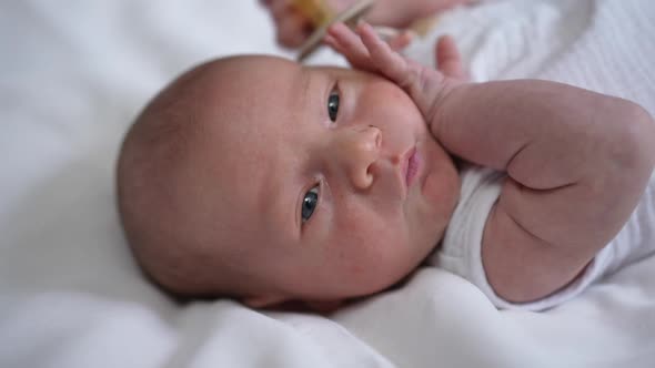 Headshot Portrait of Cute Caucasian Newborn Infant with Grey Eyes Lying on Bed Looking Away