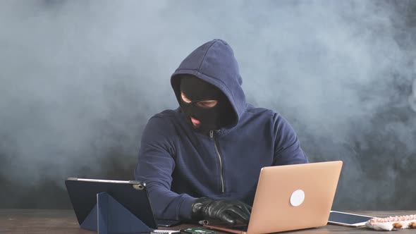 Young Anonymous Hacker Man with Laptop Isolated Over Smoky Colorful Space