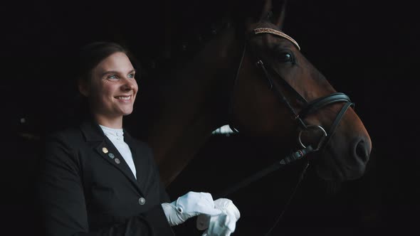 Horsewoman Standing With Her Dark Brown Horse Smiling And Putting On Her Gloves