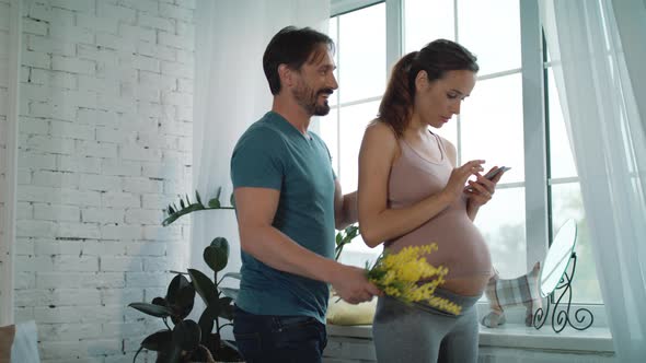 Husband Giving Yellow Flowers To Surprised Pregnant Wife at Home.