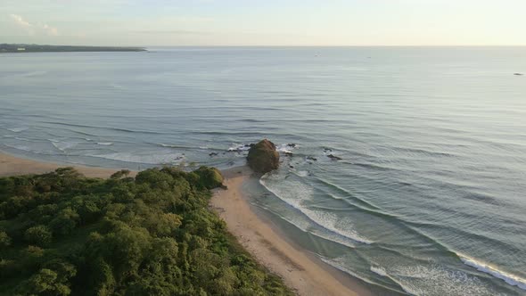 Drone approaching a large rock on the tip of a peninsula at a heavenly beach in Costa Rica. Vibrant