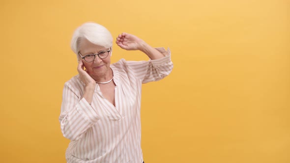 Happy Old Woman Dancing with Wireless Headphones, Isolated on Orange Background