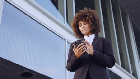 Businesswoman With Afro Using Smartphone Outside Office