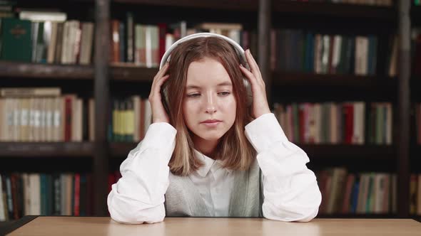 A Beautiful Small Teen Female in a Library While Listening to Music with Headphones and Daydreams