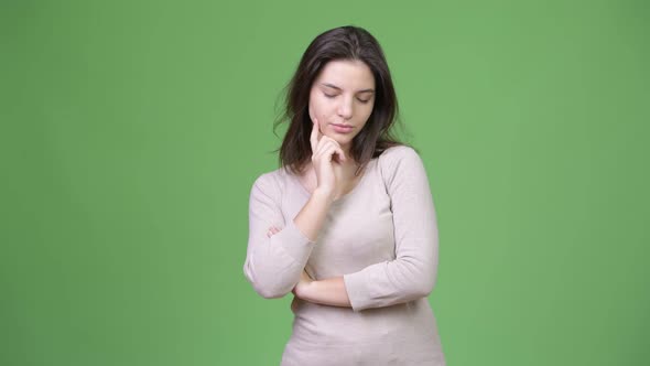 Young Beautiful Woman Thinking While Looking Down Against Green Background