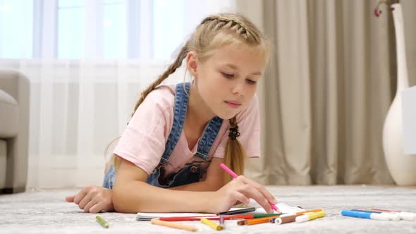 Cute Preteen Girl Lying on Floor and Drawing on Paper in Living Room