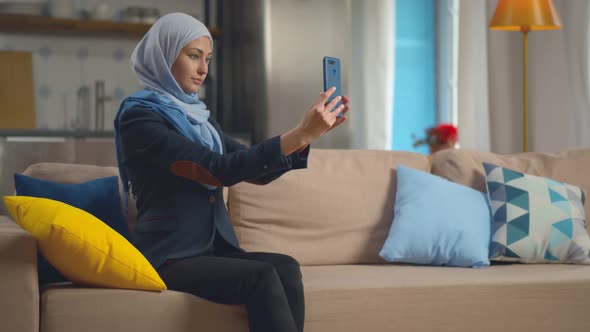 Arab Girl In Hijab Taking Photo On Smartphone Relaxing On Comfortable Couch In Living Room