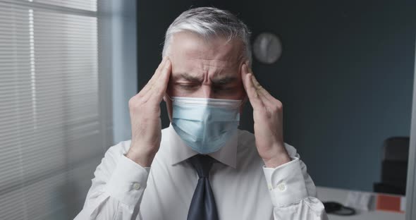 Businessman with face mask massaging his temples