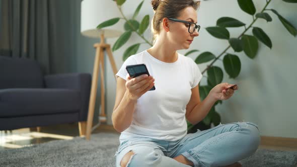 Woman with Glasses is Sitting on the Floor and Makes an Online Purchase Using a Credit Card and