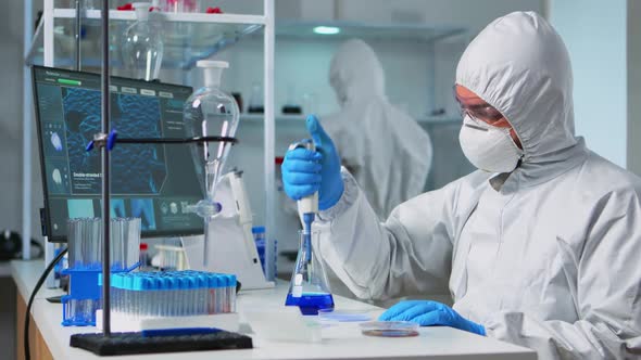 Chemist in Ppe Suit Using Micropipette for Filling Test Tubes