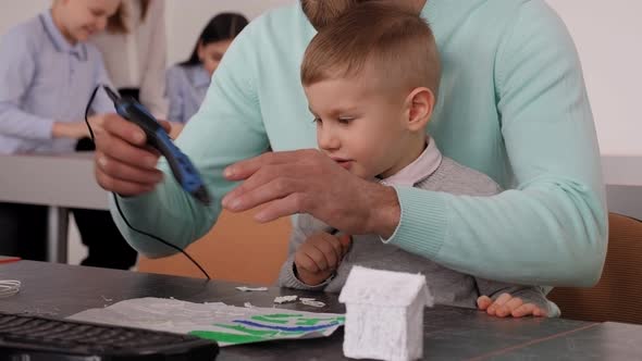 A Father and His Young Son Draw with a 3d Pen on Paper Create a Model of a Toy