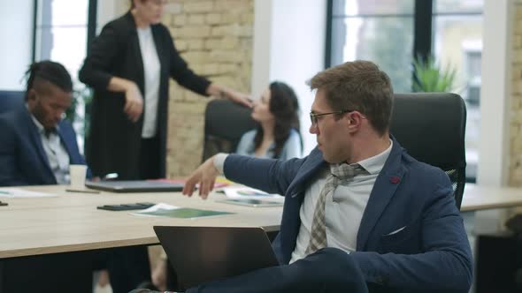 Handsome Confident Caucasian Man in Eyeglasses Analyzing Startup with Blurred Colleagues Talking at