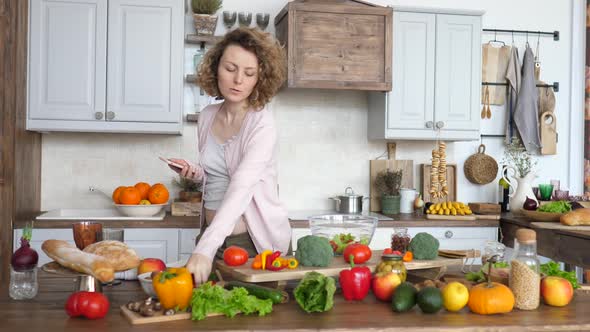 Young Pregnant Woman Looking For Recipe On Smartphone And Making Salad On Kitchen.